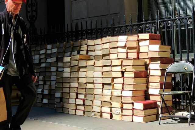 a guy walks by a bunch of stacked books on a Brooklyn sidewalk